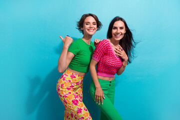 Wall Mural - Photo of shiny excited girls dressed colorful outfits showing thumb empty space isolated blue color background