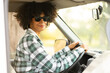 © Guirado - young African black woman driving her camper van in a road trip at autumn looking at camera