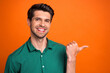 Leinwandbild Motiv Photo of cheerful cute guy wear green shirt pointing thumb empty space isolated orange color background