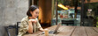 Portrait of asian woman looking at laptop, video chat, talking with someone via computer camera, sitting in cafe and drinking coffee, online meeting