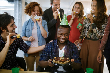 Young and diverse group of people celebrating a surprise birthday party in the office of a startup company