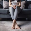 © Vikash Kumar - An unrecognizable barefooted woman in dark grey leggings and top sitting by the couch on beige carpet embracing her legs. House, home, carpet,  home decor. Created with Generative AI Technology.