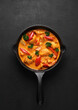 Chicken paprikash dish with paprika, onion, sweet pepper in black pan on dark table. top view