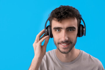 Poster - Young brunette man in headphones on blue background, closeup