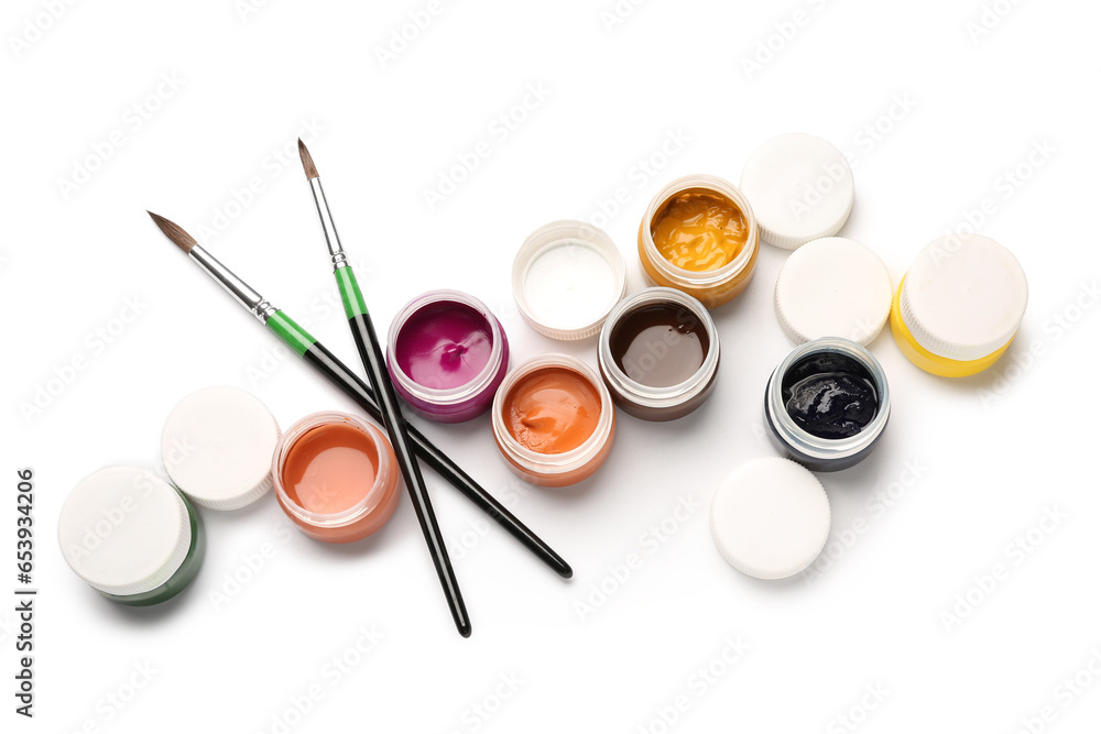 Jars of colorful gouache paints with brushes on white background