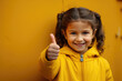 A cute little girl wearing a yellow jacket giving a thumbs up gesture. This image can be used to represent positivity, approval, success, or encouragement in various projects and designs.