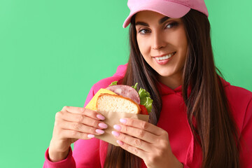 Wall Mural - Young woman with tasty sandwich on green background, closeup