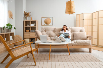 Wall Mural - Young woman reading magazine on couch in living room