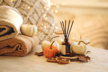 Autumn mood, cozy fall home atmosphere. Aroma diffuser, pumpkins, knitted warm sweaters, burning candles, dry leaves on wooden table. Concept of house decor, apartment seasonal fragrance. Thanksgiving