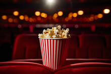 Close Up A Popcorn In Paper Stripped Bucket On Red Soft Armchair On Blurred Empty Cinema Hall