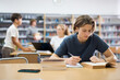© JackF - Portrait of teenager reading books and writing in notebooks in the library