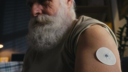 close-up shot of elderly caucasian man putting blood sugar monitor patch onto his shoulder, to measu