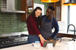 Happy diverse couple baking together in kitchen, using tablet at home