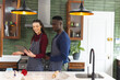 Happy diverse couple baking together in kitchen, using tablet at home, copy space