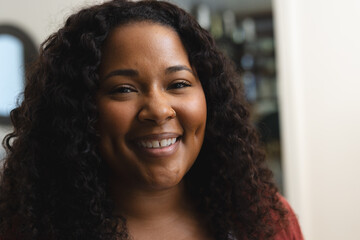 Head of happy african american woman with curly hair smiling in sunny house