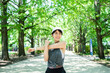 Young Asian woman stretching arms and shoulders while running in a park in the morning. Health and fitness training, healthy living lifestyle, well-being.