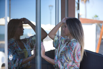 Young and beautiful woman in a sequined dress, looking at her reflection in the glass of a shop window, calm and relaxed. Concept beauty, fashion, trend, tranquility.