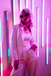 Leinwandbild Motiv Young beautiful hipster woman in street style fashion concept. Hot model wearing white suit and sunglasses. Female posing in pink and blue neon light in studio interior