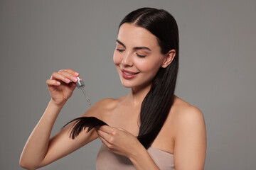 Sticker - Beautiful woman applying hair serum on grey background. Cosmetic product