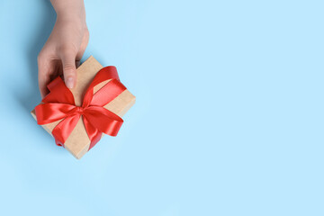 Wall Mural - Woman holding gift box with red bow on light blue background, top view. Space for text