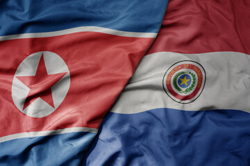 big waving realistic national colorful flag of north korea and national flag of paraguay .