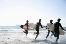 Back view of surfers running in the sea holding surfboards
