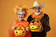 Pareja de hombre y mujer mayores disfrazados para halloween, con cestas llenas de calabazas y caramelos  sobre fondo naranja