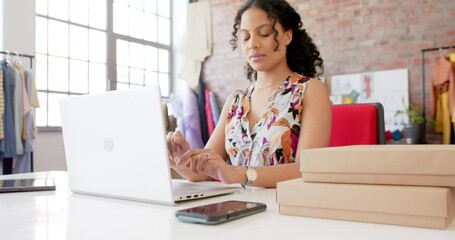Wall Mural - happy biracial female fashion designer using laptop and smartphone in studio, slow motion