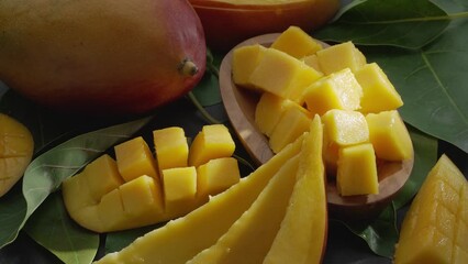 Wall Mural - Ripe mango fruits with slices and mango leaves slowly move in the frame on a gray stone table. Nice fruit background for your projects. Macro video shooting.