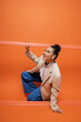 © LIGHTFIELD STUDIOS - cheerful african american fashion model in stylish outfit squatting out of orange framework