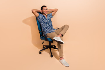 Wall Mural - Full length photo of dreamy cheerful man wear print shirt sitting office armchair arms behind head isolated beige color background