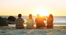 Four Friends On The Beach Watching The Sunset And Raising Glasses