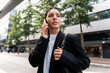 © Andrei - Wide portrait of siren businesswoman in black suit holding a phone to ear looking away in modern city street