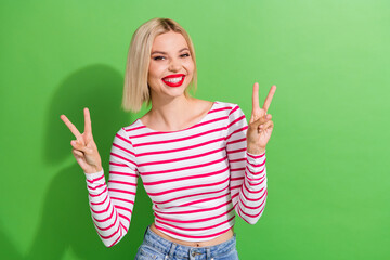 Poster - Portrait of lovely adorable cheerful girl with short hairdo wear stylish clothes showing v-sign isolated on green color background