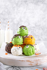 Homemade funny monster mini cakes or cake pops in a colored chocolate glaze and sugar sprinkles. Halloween treat on a concrete background.