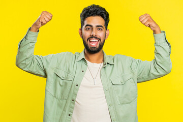 Happy joyful Indian man celebrating success victory, winning birthday, lottery jackpot goal achievement play game good positive news, triumph. Young Arabian guy isolated on yellow studio background