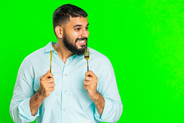 Ready to eat. Hungry Indian man waiting for serving dinner dishes with with restlessness holding cutlery fork knife, will appreciate delicious restaurant meal. Guy isolated on chroma key background