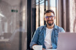 © kerkezz - Handsome smiling young man drinking coffee sitting at office desk and looking at camera