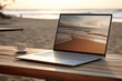 © barmaleeva - Open laptop on wooden table. Work space outdoors with view on the ocean. Office on the beach. Generative AI
