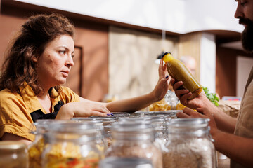 Canvas Print - Vendor showcasing her products in zero waste marketplace venue, trading preservatives free food to interested customer. Local farmer selling environmentally friendly bulk products during event to