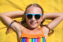 Happy Little Girl In Sunglasses Lying On Beach Towel Outdoors, Top View