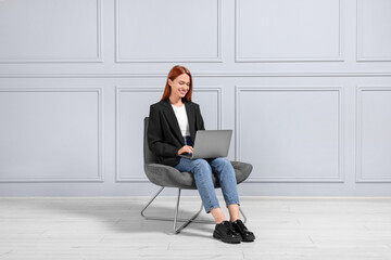 Sticker - Happy young woman with laptop sitting in armchair near light grey wall indoors