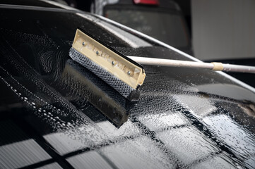 Someone using a glass wiper for cleaning a car windshield. It’s important to keep a car’s front window clear of any visual obstruction for safe driving and to keep the car presentable.