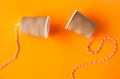 DIY paper cups with string on orange background. Concept, telephone toys which apply with science knowledge about vibration sound through straining strings causing us to hear the sound.               