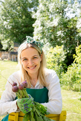 pretty young woman harvests radishes in her own garden and is happy and satisfied and is smiling