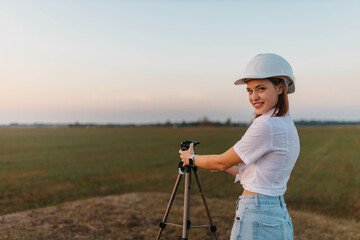 female engineer surveyor in a white helmet with a tripod in the field studying the location for the construction of a building