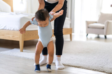 Portrait of enjoy happy love family asian mother playing and teaching help adorable little asian baby learning to walk.Mom help first step with cute son beginnings development at home.Love of family 