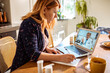 © Marko Geber - Young woman consulting her doctor on a video call from a laptop in the kitchen at home