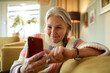 © Marko Geber - Senior Caucasian woman using her smartphone on the couch at home