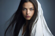 Close-up portrait of a very beautiful young woman with green eyes, and long dark brown hair, wearing a white top and a white veil or head covering - copy space, isolated, blue background